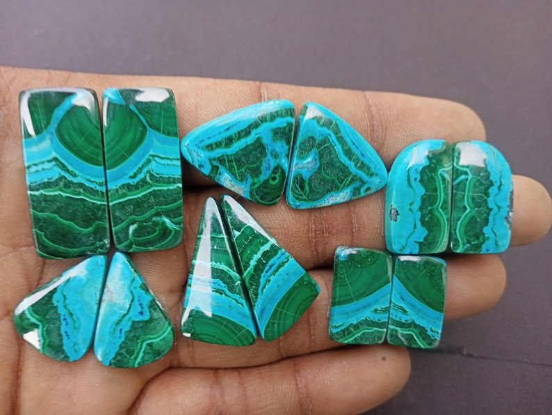 May include: A set of eight cabochon gemstones, cut in various shapes, including rectangular, triangular, and oval. The stones are a vibrant mix of green and blue, with intricate patterns and swirls.