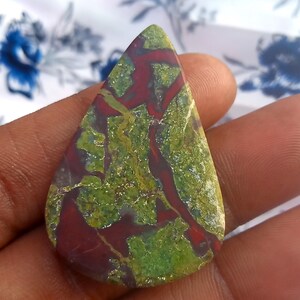 K&ouml;nnte beinhalten: Ein tropfenf&ouml;rmiger Cabochon aus gr&uuml;nem und rotem Jaspis mit einem wirbelnden Muster.