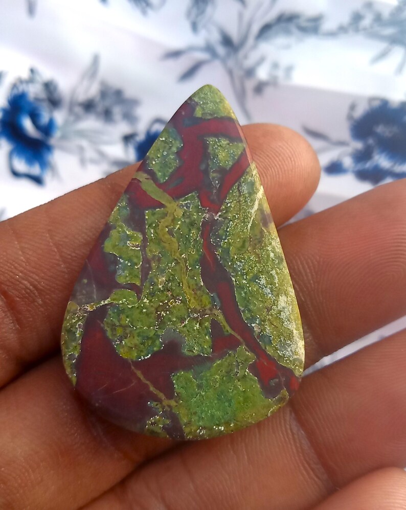 K&ouml;nnte beinhalten: Ein tropfenf&ouml;rmiger Cabochon aus gr&uuml;nem und rotem Jaspis mit einem wirbelnden Muster.