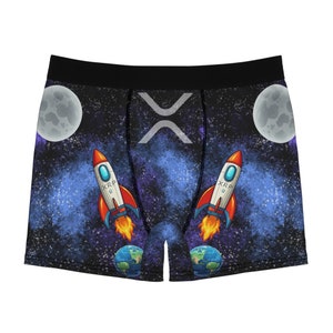 Peut inclure: Boxer noir avec un imprimé sur le thème de l'espace représentant une galaxie bleue, des étoiles, des planètes et deux fusées avec le texte "XRP" dessus.