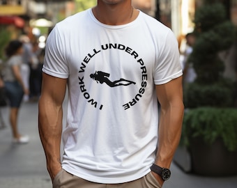 Könnte beinhalten: Weißes T-Shirt mit einem schwarzen Kreis-Motiv, auf dem "Ich arbeite gut unter Druck" steht und eine Taucher-Silhouette abgebildet ist.