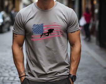 Puede incluir: Una camiseta gris con un diseño de bandera estadounidense desgastado que presenta una silueta de buceador. La bandera es roja, blanca y azul.