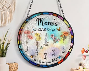 May include: A round stained glass window hanging with a black metal frame. The window features a colorful floral design with butterflies and the text "Mom's Garden" and "We love you lots".