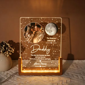 May include: A rectangular acrylic night light with a wooden base featuring a circular photo of a child and adult, a moon graphic, and the text: Daddy, The day you became my hero and my forever. I love you to the Moon and back. Love, Olivia.