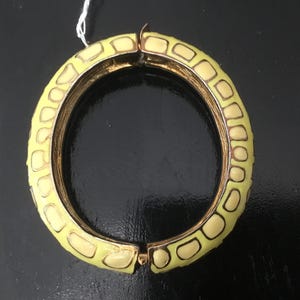 May include: A yellow and gold bangle bracelet with a textured design. The bracelet is open and ready to be worn.