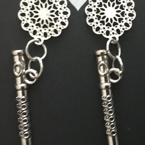 May include: A pair of silver earrings with a filigree design and a long, cylindrical charm. The charms have a repeating pattern of small circles.