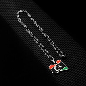 May include: A silver chain necklace with a pendant shaped like the outline of Libya. The pendant is colored with the Libyan flag, featuring a green, black, and red design with a white crescent moon and star.