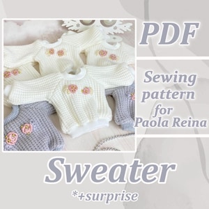 May include: A collection of white and grey doll sweaters with floral embroidery. The sweaters have a waffle knit texture and are designed for Paola Reina dolls. The image also includes the text "PDF Sewing pattern for Paola Reina Sweater *+surprise."