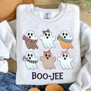Op de afbeelding: Lichtgrijs sweatshirt met zes cartoongeesten met strikken en sjaals met patronen. Het woord "BOO-JEE" is in het zwart gedrukt. De geesten hebben zwarte ogen en lachende gezichten.