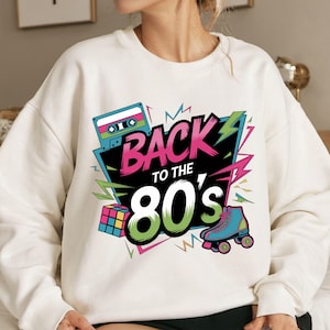 May include: White sweatshirt with a colorful graphic design featuring the text "Back to the 80's" with a cassette tape, a Rubik's cube, and roller skates.