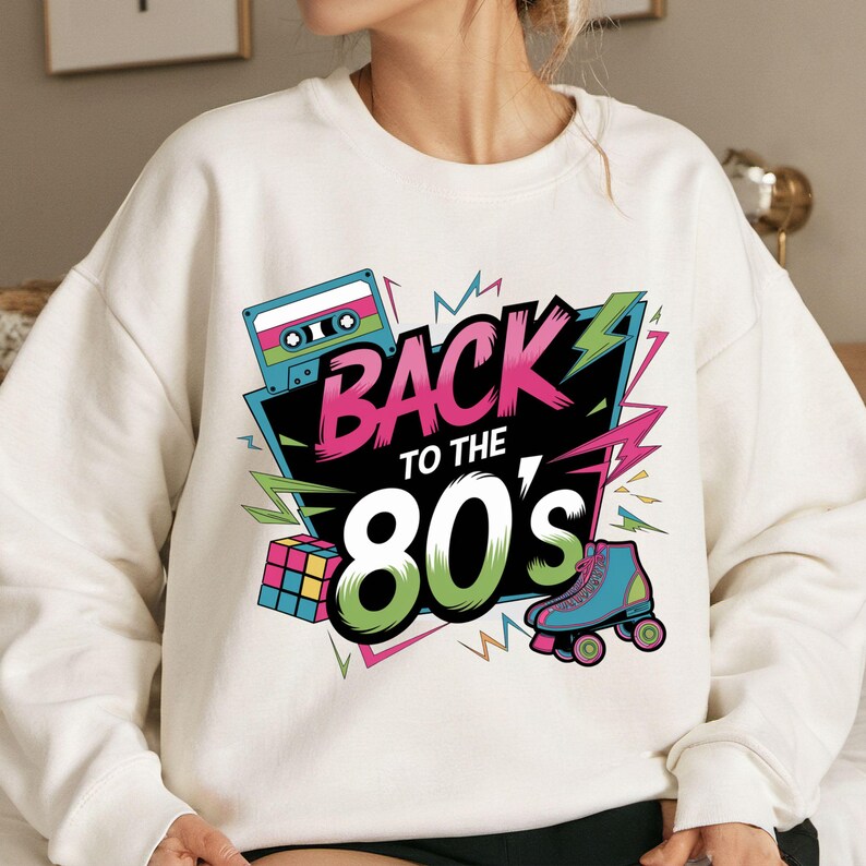 May include: White sweatshirt with a colorful graphic design featuring the text "Back to the 80's" with a cassette tape, a Rubik's cube, and roller skates.