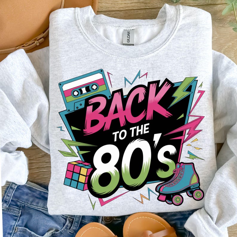 May include: A gray sweatshirt with a retro 80s design featuring a cassette tape, a Rubik's cube, roller skates, and the text "Back to the 80's".