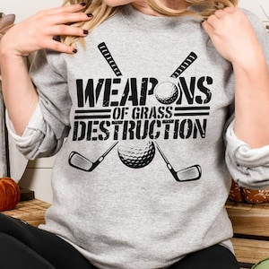 May include: Gray sweatshirt with a black graphic design that says "Weapons of Grass Destruction" with a golf ball and two golf clubs.