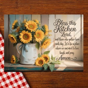 May include: A decorative kitchen sign featuring a bouquet of sunflowers in a white pitcher with a blue ribbon. The sign includes the text "Bless this Kitchen Lord" and a prayer. The background has a rustic, farmhouse style.