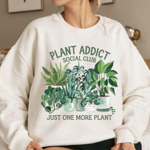 May include: White sweatshirt with a green graphic of potted plants and the text "Plant Addict Social Club Just One More Plant".