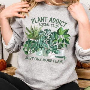 May include: Gray sweatshirt with the text "Plant Addict Social Club" and a graphic of potted plants. The text "Just One More Plant" is below the graphic.