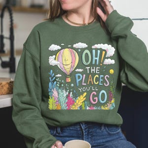 May include: A green sweatshirt with a colourful graphic of a hot air balloon and the text "Oh! The Places You'll Go".