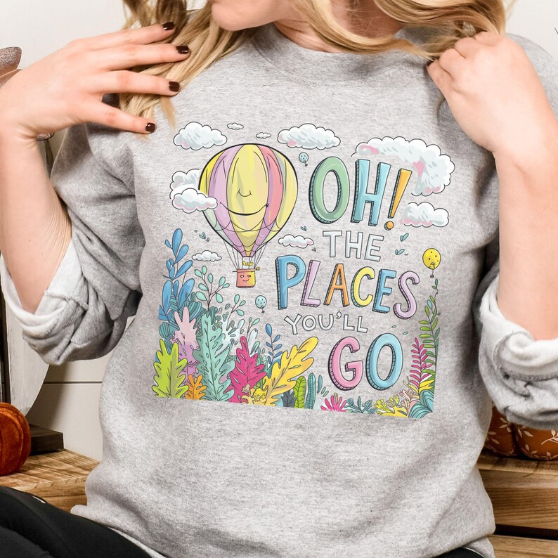 May include: A grey sweatshirt featuring a colourful illustration of a hot air balloon, clouds and foliage. The text "Oh! The Places You'll Go" is printed on the sweatshirt.