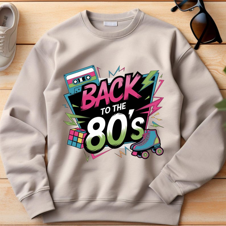 May include: A beige sweatshirt with a graphic print of a cassette tape, a Rubik's cube, roller skates, and the text "Back to the 80's".