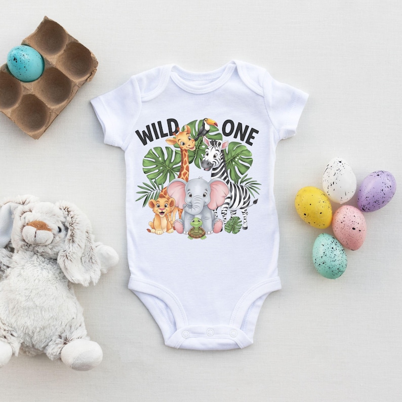 May include: White baby onesie with a green, yellow, and black jungle animal print. The onesie says "Wild One" in black text.