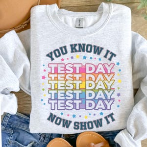 May include: A gray sweatshirt with the text "You know it Test Day Now show it" in a rainbow color scheme with stars around the text.
