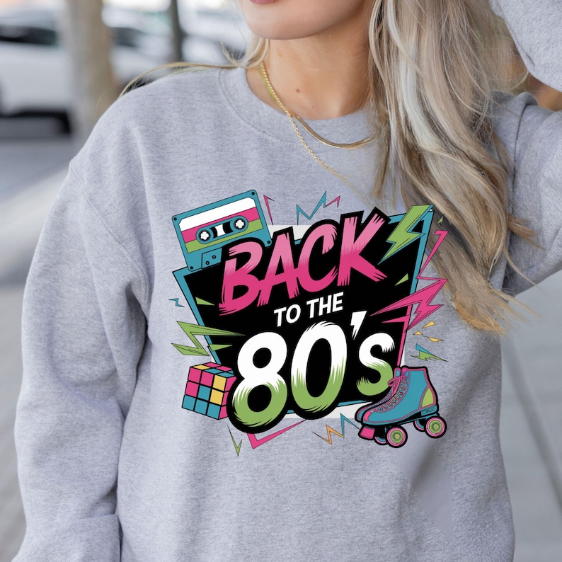 May include: A gray sweatshirt with a colorful graphic design featuring the text "Back to the 80's" with a cassette tape, a Rubik's Cube, and roller skates.