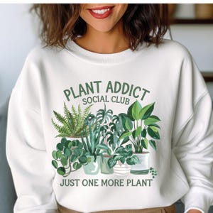 May include: White sweatshirt with a green graphic of potted plants and the text "Plant Addict Social Club" and "Just One More Plant".