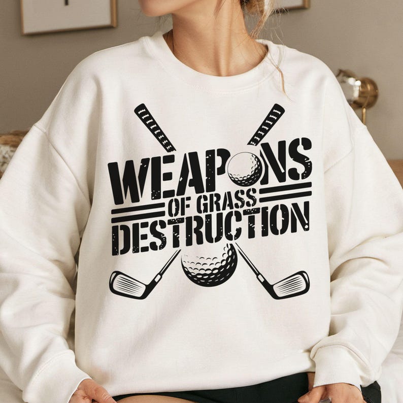 May include: White sweatshirt with a black graphic design of two crossed golf clubs and a golf ball. The text reads "Weapons of Grass Destruction."