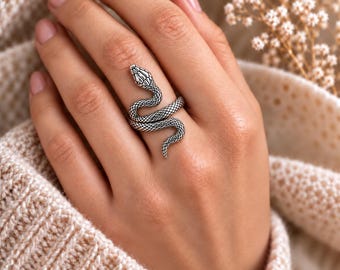 May include: A silver-toned metal ring shaped like a coiled snake with detailed scale textures. The snake's head rests near the knuckle, while its body wraps around the finger, creating a continuous, winding design with an oxidized finish.