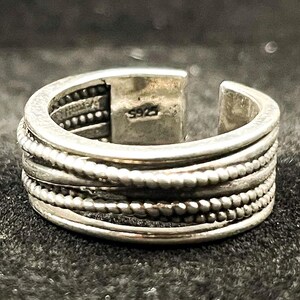 May include: A silver-toned open band ring featuring a multi-layered design with alternating smooth and beaded wire textures. The interior of the band is clearly stamped with the text S925, indicating the metal composition of this adjustable ring.