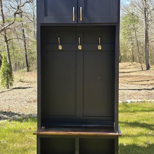 May include: Black wooden entryway bench with a storage shelf and two cabinets with gold handles. The bench has a brown top and a small shelf below.