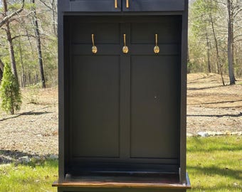 May include: Black wooden entryway bench with a storage shelf and two cabinets with gold handles. The bench has a brown top and a small shelf below.