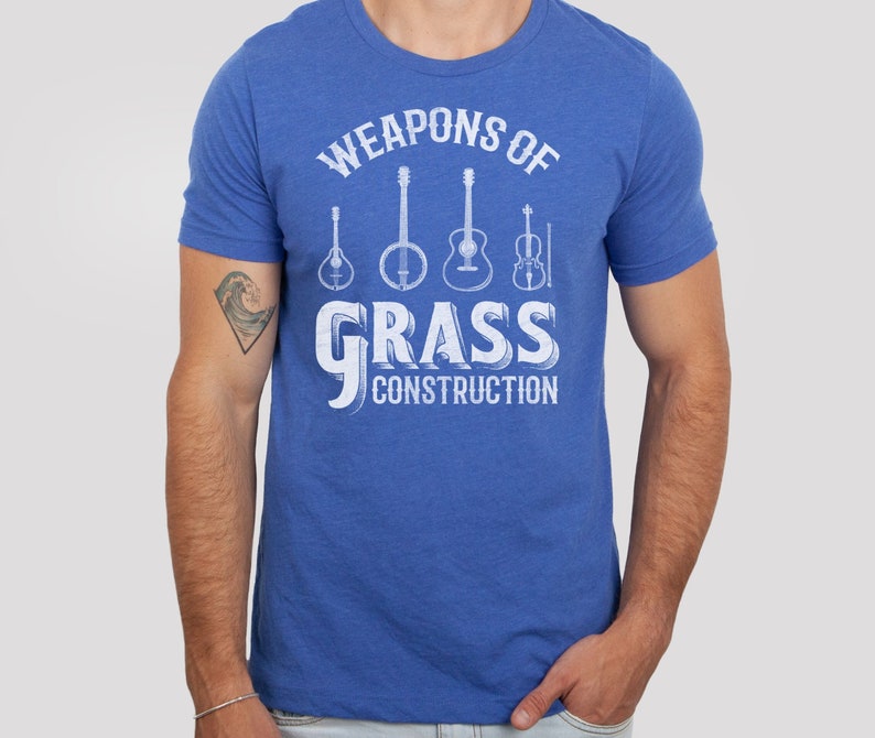 Op de afbeelding: Een koninklijk blauw t-shirt met een witte afbeelding van muziekinstrumenten en de tekst "Weapons of Grass Construction".