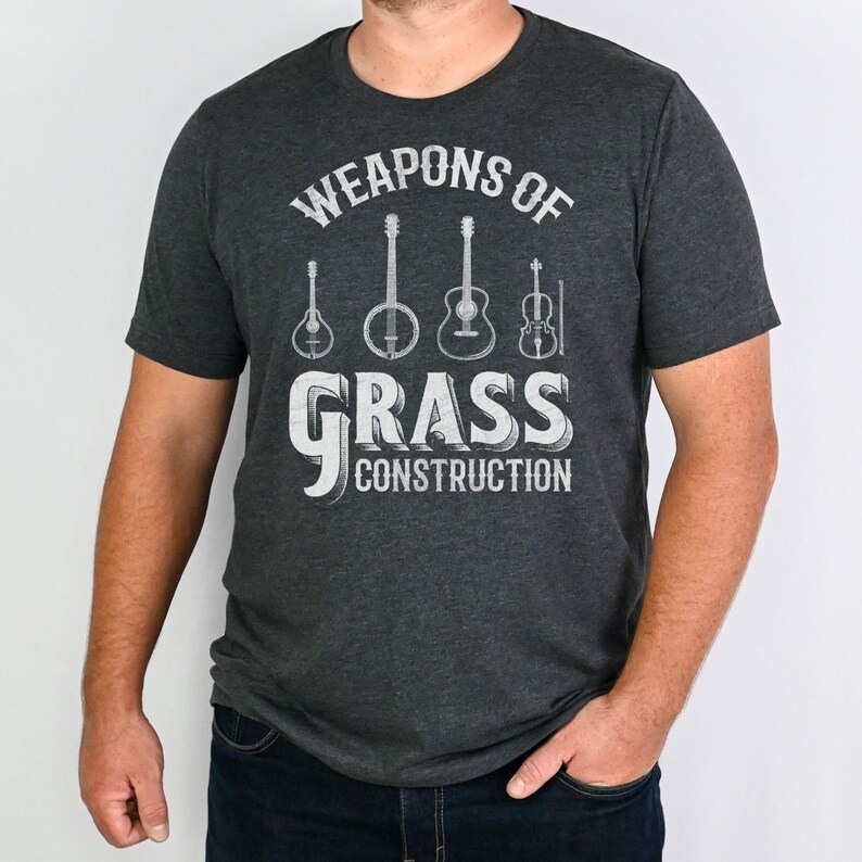 Op de afbeelding: Een donkergrijs T-shirt met een witte afbeelding van muziekinstrumenten en de tekst "Weapons of Grass Construction".