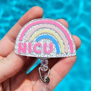 May include: A silver glitter rainbow with a pink "NICU" inscription, attached to a clear retractable badge holder.