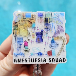 May include: A white glitter badge reel with a colorful illustration of medical equipment and the text "Anesthesia Squad".