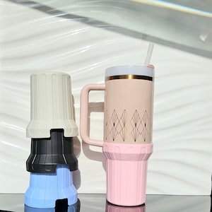 Puede incluir: Dos vasos térmicos, uno rosa con un diseño geométrico dorado y una tapa blanca, y otro conjunto de tres vasos apilados en blanco, negro y azul.