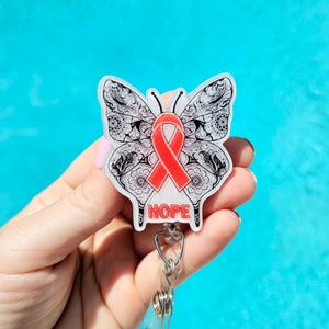 May include: A white butterfly-shaped badge holder with a red ribbon and the word "HOPE" printed on it. The butterfly has intricate black and white details.