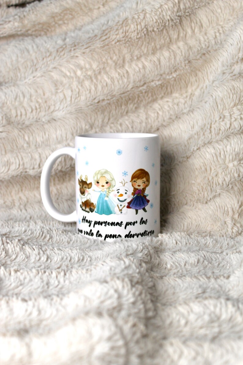 Puede incluir: Taza de cer&aacute;mica blanca con una ilustraci&oacute;n colorida de Elsa, Anna y Olaf de la pel&iacute;cula Frozen. La taza tiene un texto negro que dice "Hay personas por las que vale la pena derretirse".