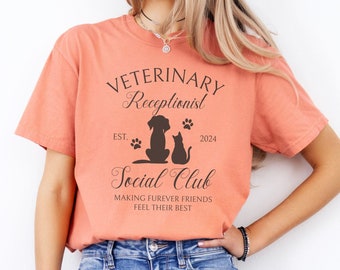 Könnte beinhalten: Ein terracottafarbenes T-Shirt mit dem Text "Veterinary Receptionist" und "Social Club" mit einer Silhouette eines Hundes und einer Katze. Der Text enthält auch "Est. 2024" und "Making furever friends feel their best."