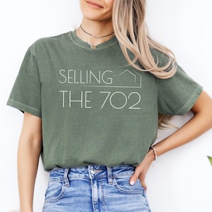 May include: A green t-shirt with the text "SELLING THE 702" in white. The shirt is made of a soft, comfortable material and has a relaxed fit.