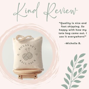 May include: A white canvas tote bag with black text and a yarn ball graphic. The text reads "Roxanne's Ball Sack". The bag is sitting on a wooden stool. The image includes a customer review that reads "Quality is nice and fast shipping. So happy with how my tote bag came out. I use it everywhere!" -Michelle B.