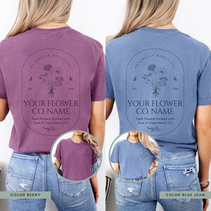 May include: Two short-sleeved t-shirts, one berry-colored and one blue jean, feature a floral design with text. The design includes the words "NATURALLY BEAUTIFUL", "YOUR FLOWER CO. NAME", and "fresh flowers farmed with love in Carpinteria, CA".