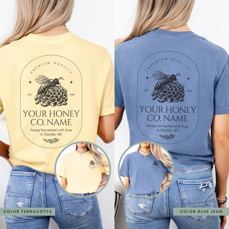 May include: Two t-shirts featuring a honey bee design. The t-shirts are in terracotta and blue jean colours. The design includes a bee, honeycomb, and the text "Your Honey Co. Name" with the tagline "honey harvested with love in Gackle, ND".