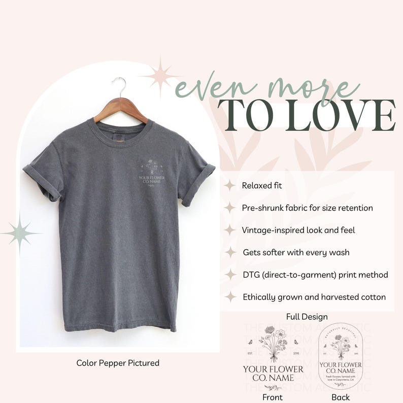 May include: A gray t-shirt with rolled-up sleeves hangs on a wooden hanger. The shirt features a small floral design and text on the front. The text "even more TO LOVE" is at the top. The color of the shirt is "Pepper".