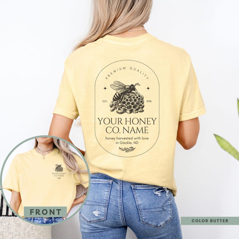 May include: A yellow t-shirt with a bee and honeycomb design on the back. The design includes the text "PREMIUM QUALITY", "EST. 1998", "YOUR HONEY CO. NAME", "honey harvested with love in Gackle, ND". The front of the shirt has a smaller version of the bee and honeycomb design with the text "YOUR HONEY CO. NAME".