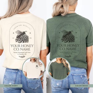 May include: Two t-shirts with a vintage-style logo featuring a bee and honeycomb. The text on the logo reads "Premium Quality", "Est. 1998", "Your Honey Co. Name", and "Honey harvested with love in Gackle, ND". The t-shirts are available in ivory and moss green.
