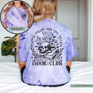 May include: Purple tie-dye t-shirt with a black graphic design featuring a book, snake, skull, and flowers. The text on the shirt reads "Always Fallin' for the Villain + Meet Weekly Dark Romance Book Club".