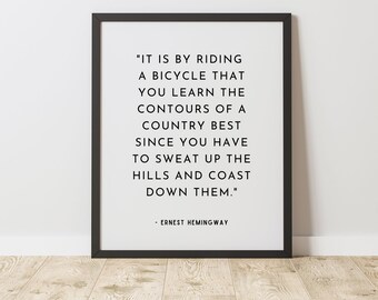 May include: Black and white typography print with a quote by Ernest Hemingway about riding a bicycle and learning the contours of a country. The quote reads, "It is by riding a bicycle that you learn the contours of a country best since you have to sweat up the hills and coast down them."