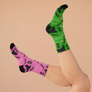 May include: A pair of socks with a green and pink design. The socks feature a black silhouette of a witch's hat and the words "KICK ASS" and "SPELL BOUND".
